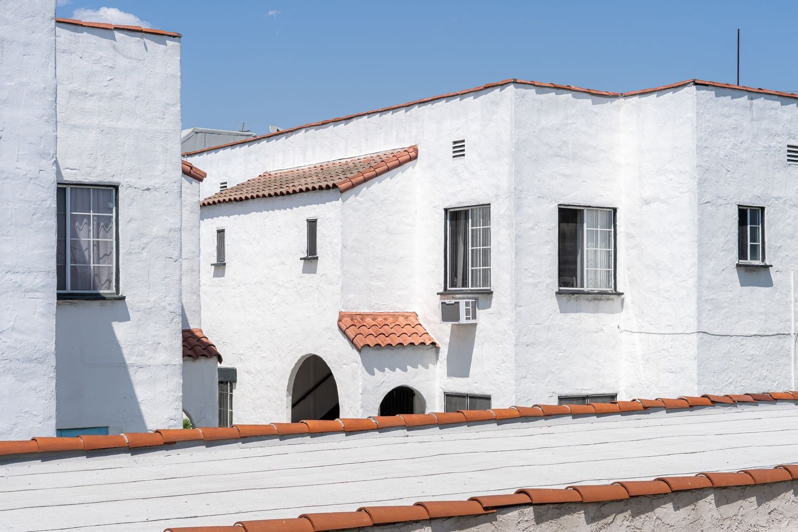 White stucco apartment buildings with terracotta roof tiles and an arched entryway.