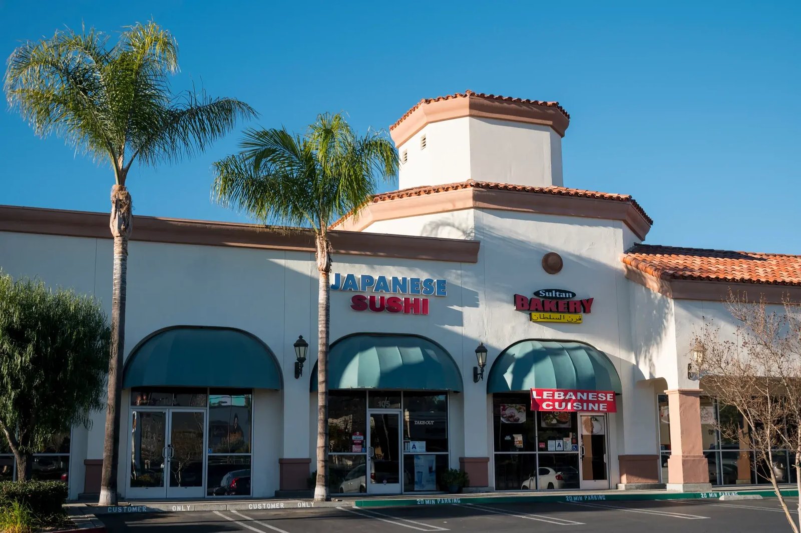 Retail storefronts with arched windows, terracotta roof tiles and palm trees.