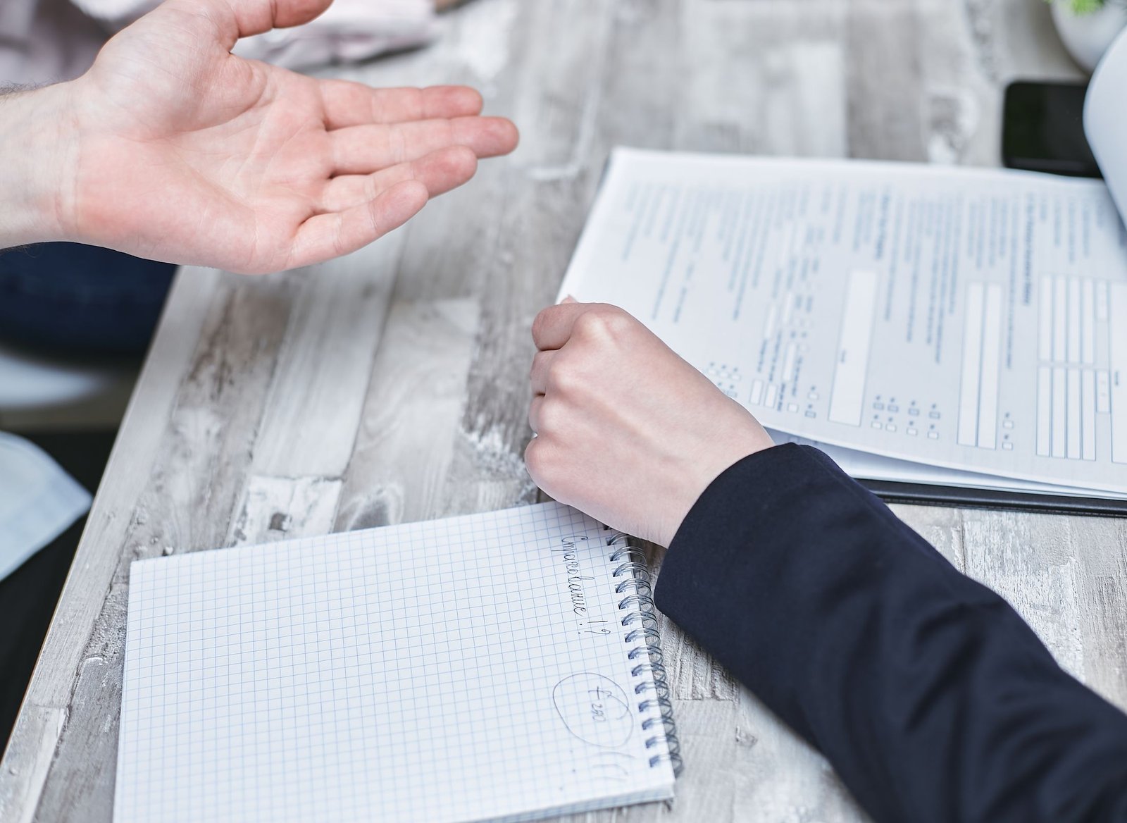 Two people gesture over printed documents and a notebook at a meeting table