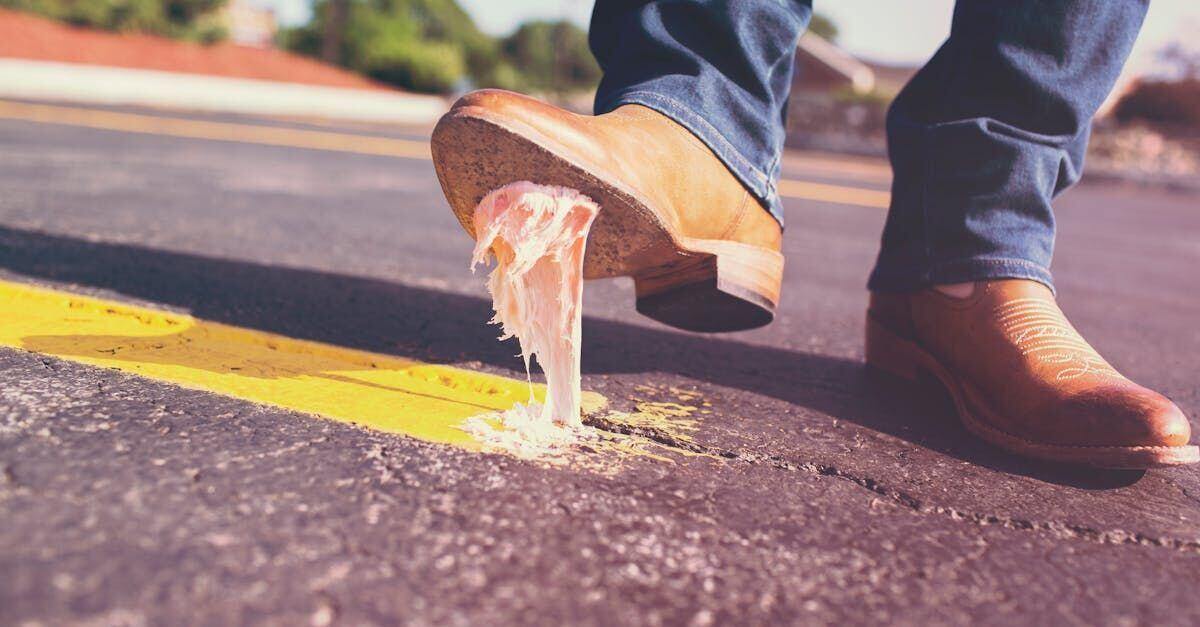 Brown leather shoes on pavement, with one sole lifting sticky gum.