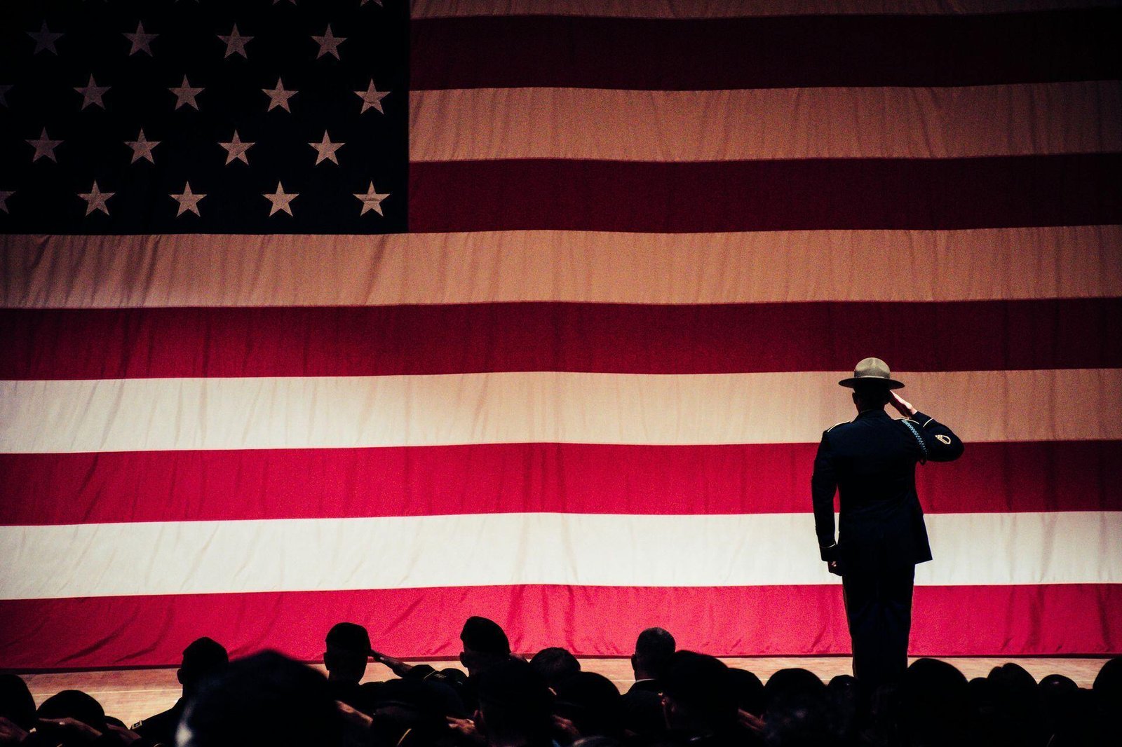 A uniformed person saluting in front of a large United States flag.