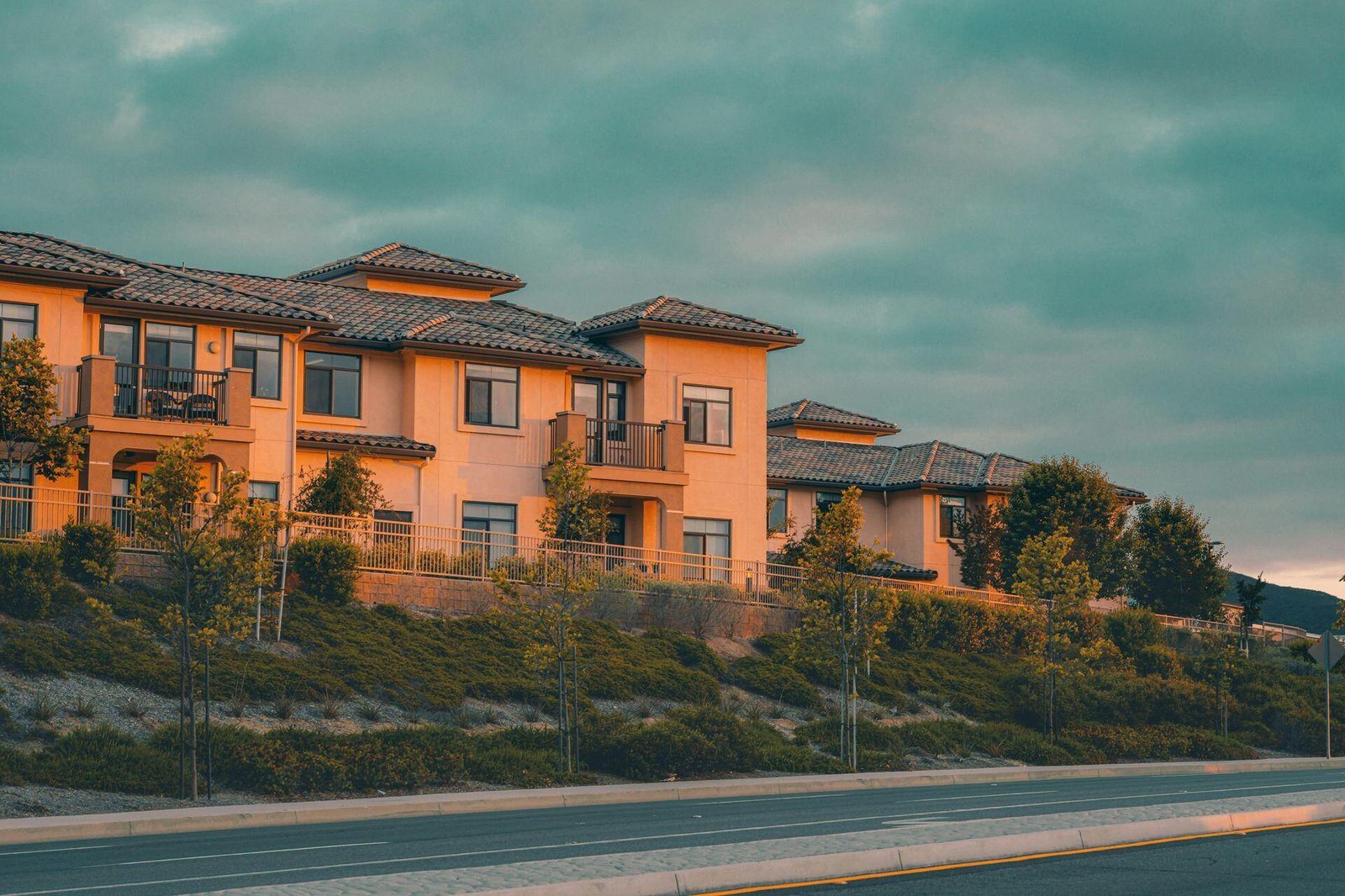Two-story residential buildings with balconies beneath a cloudy sky.