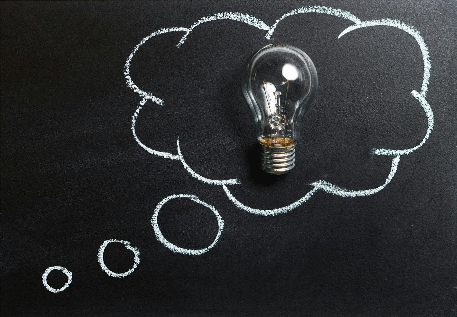 A lightbulb inside a chalk-drawn thought bubble on a dark board.