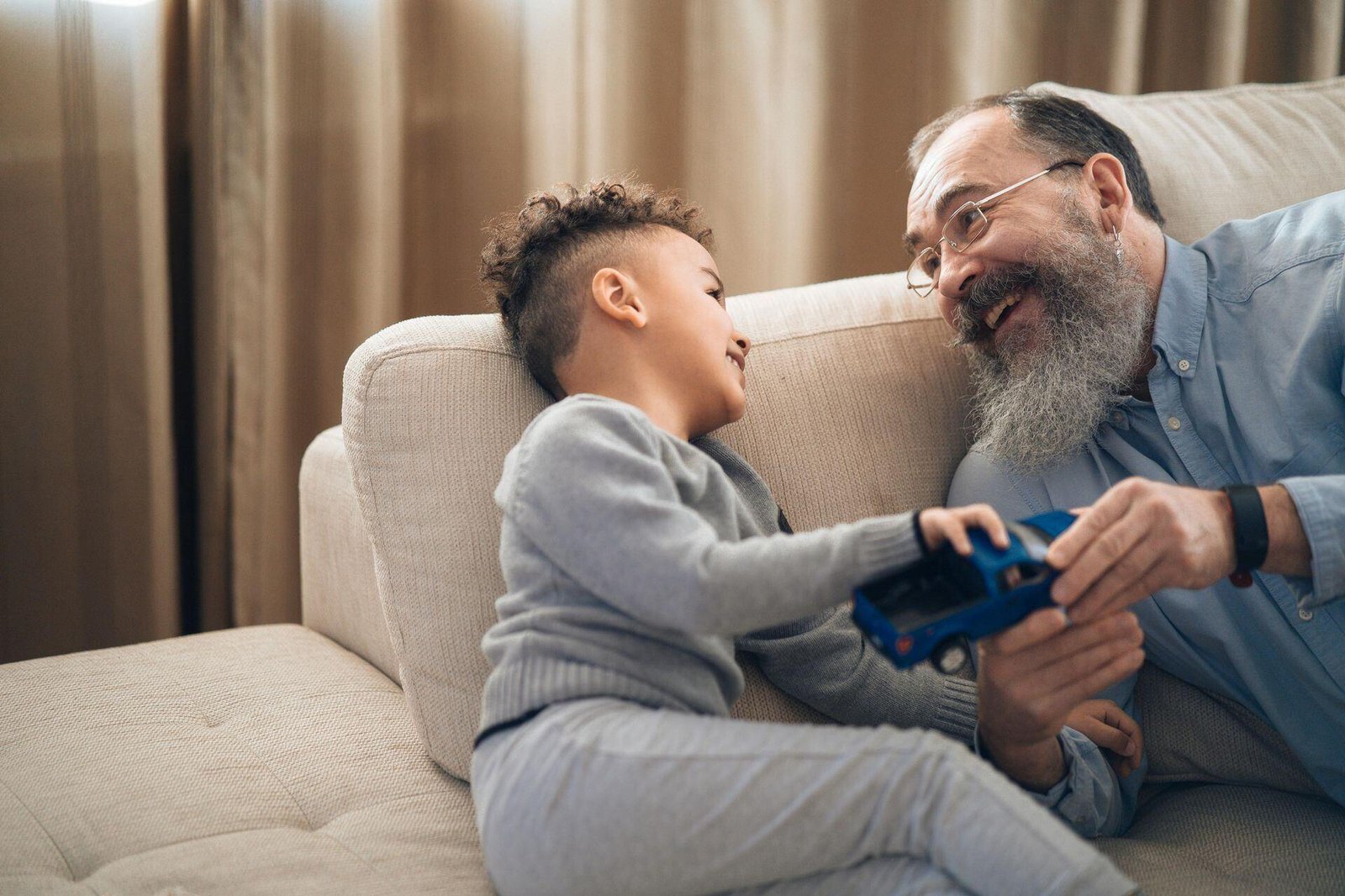 An adult and child sitting together on a sofa and playing with a toy car.