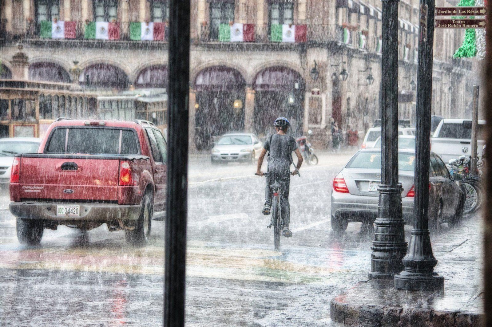 A cyclist and vehicles moving through heavy rain on a city street.