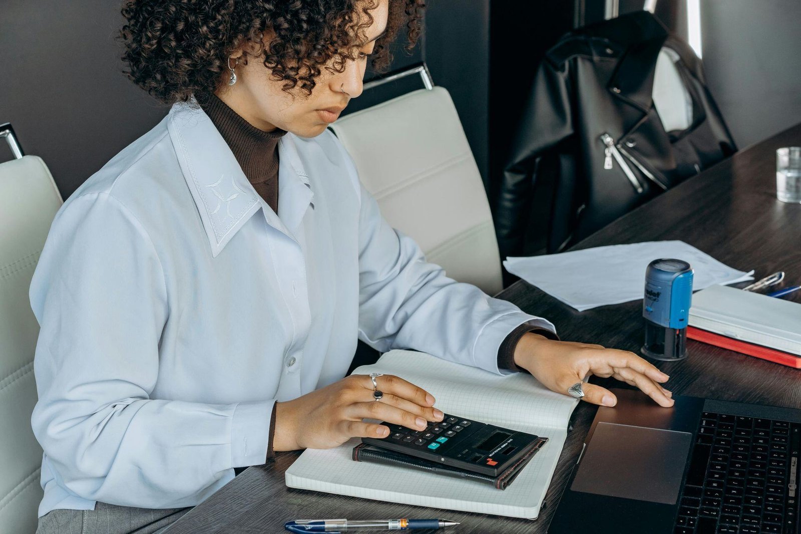 A person using a calculator on a notebook beside a laptop.