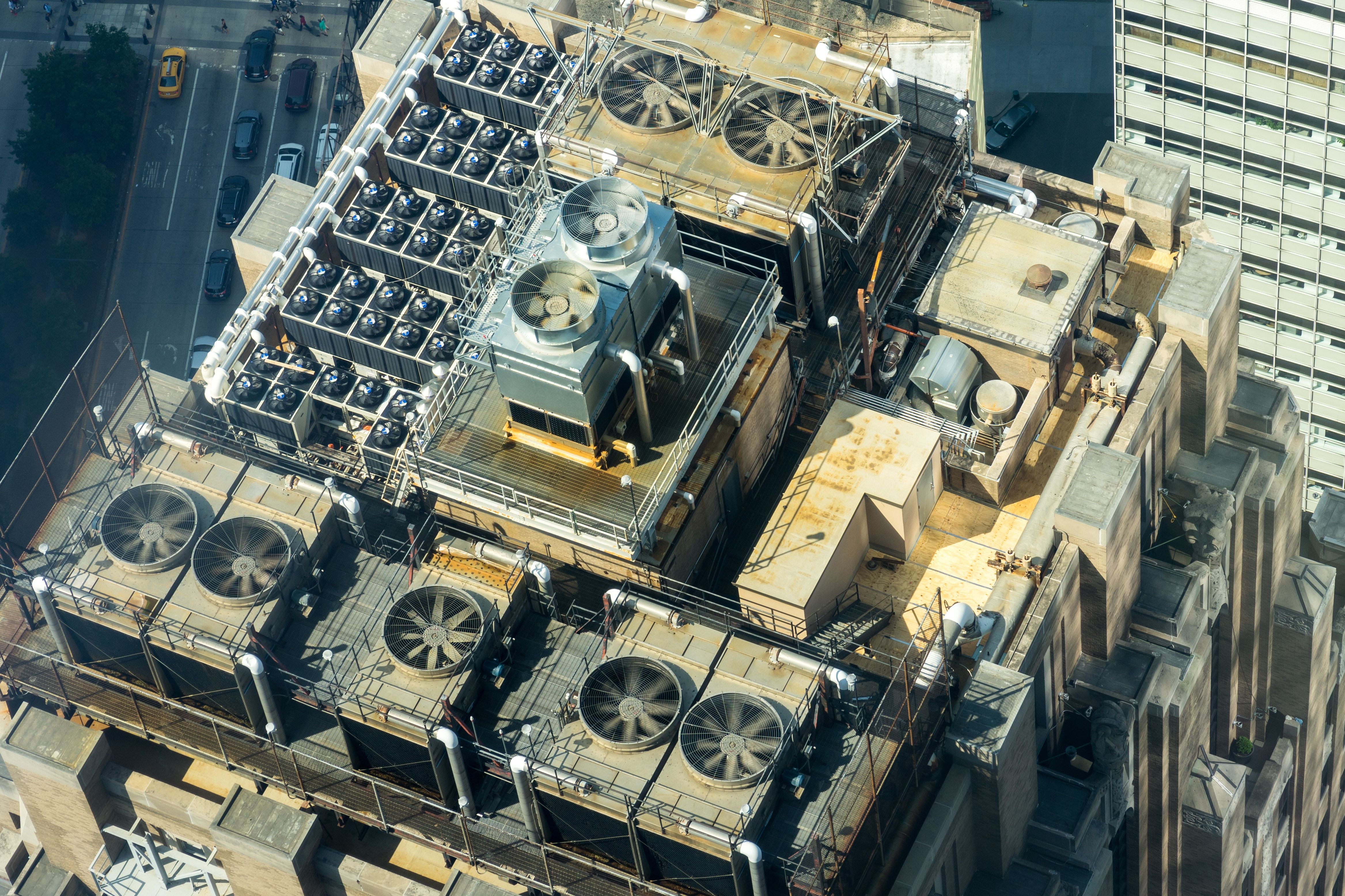 Aerial view of multiple HVAC units and ventilation equipment on a city building roof.