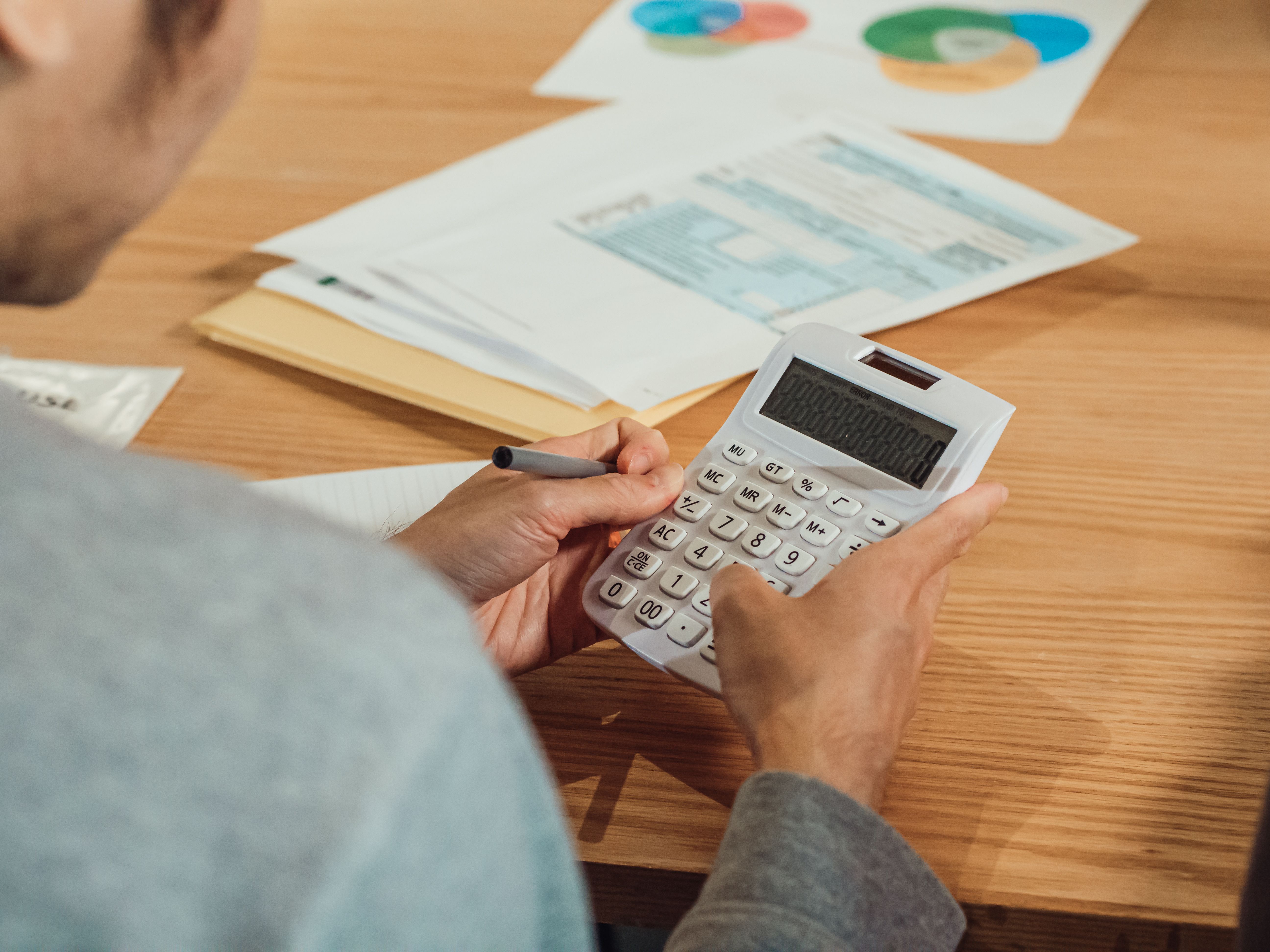 Person using a calculator beside financial documents at a desk.