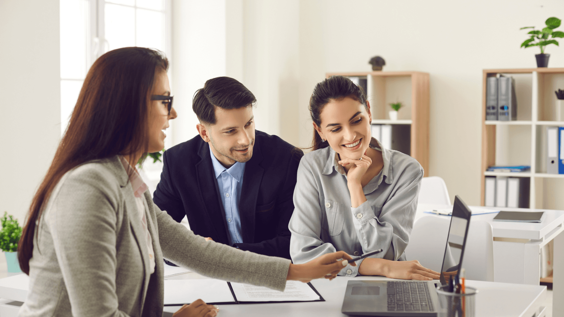 Three people discussing information at a desk with a laptop.